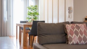 Ein modernes Wohnzimmer mit einer Couch, einem Esstisch, Stühlen, einer Topfpflanze und einem an der Wand befestigten Telefon.