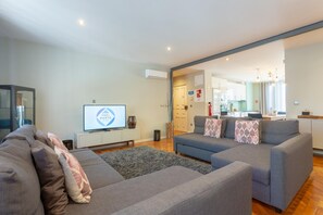 A modern living room with a grey sofa set, a flat-screen TV, and a kitchen visible through an open doorway. - Feel Porto Ruby Townhouse (Porto)