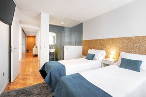 A modern hotel room with two beds, a bathroom with a large mirror, and a hallway leading to a dining area.