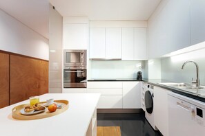 A modern kitchen with white cabinetry, a built-in oven, a microwave, a sink, and a dishwasher. - Feel Porto Downtown Poets Flat (Porto)