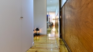 Un pasillo con suelo de madera, paredes blancas y un panel de madera a la derecha.