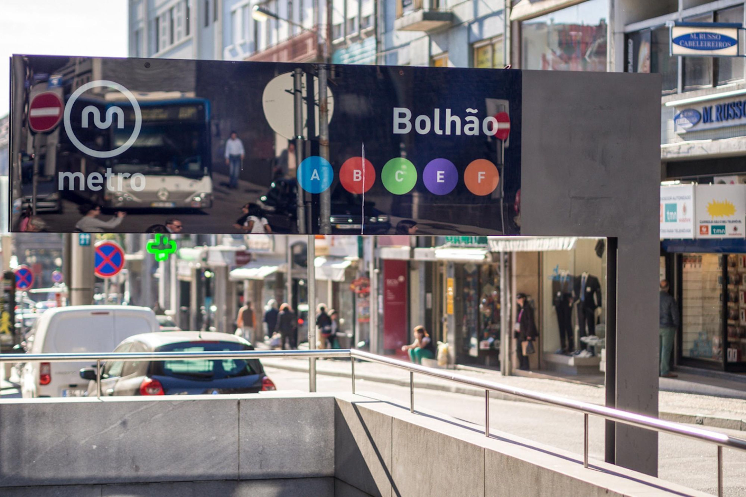 A metro sign with multiple lines and a bus in the background.