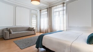 Een slaapkamer met een bed, een bank en een groot raam met gordijnen.