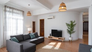 Een moderne woonkamer met een hoekbank, een flatscreen televisie, een houten salontafel en een potplant.