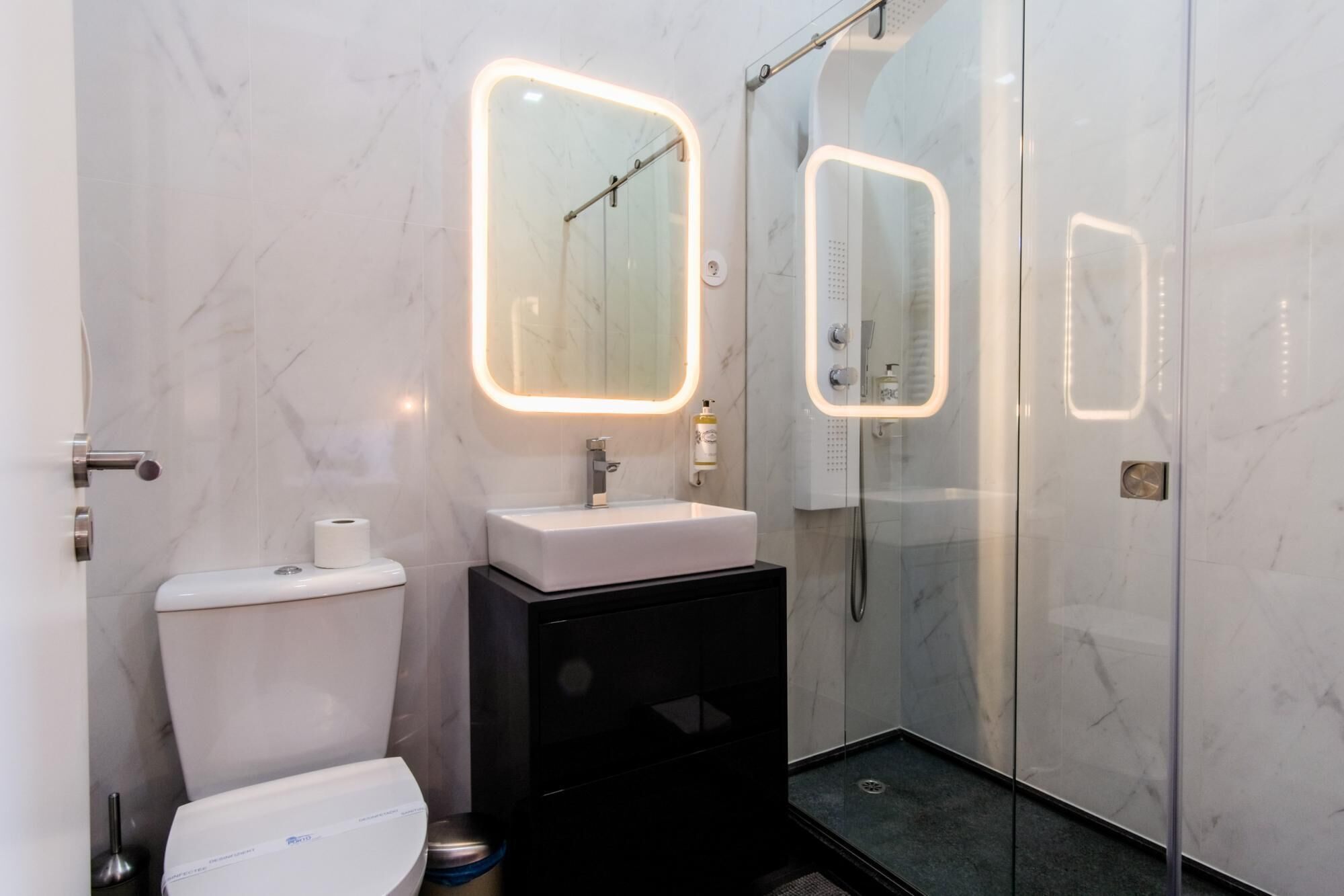 Un baño moderno con inodoro, lavamanos y cabina de ducha con paredes de vidrio.