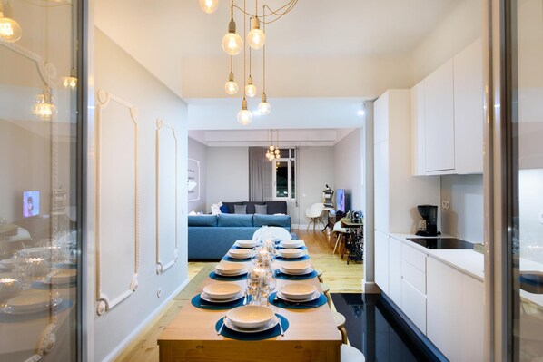 Een moderne keuken met een eettafel gedekt voor zes personen, een bank op de achtergrond en een koffieapparaat op het aanrecht.