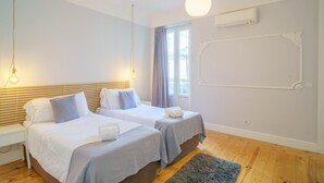 Ein Hotelzimmer mit zwei Betten, einem großen Fenster mit Vorhängen, einer Klimaanlage und Holzboden.