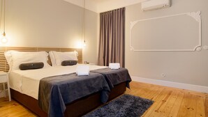 Ein Schlafzimmer mit einem hölzernen Bett, einem Nachttisch, einer Lampe an der Wand und einem großen Fenster mit Vorhängen. Eine Klimaanlage ist ebenfalls vorhanden.