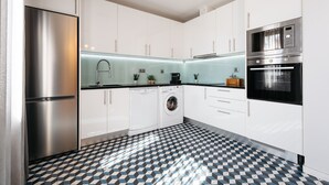 A modern kitchen with white cabinets, a stainless steel refrigerator, a washing machine, and a microwave. - Feel Porto DOC Townhouse (Porto)