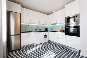 Una cocina moderna con armarios blancos, un refrigerador de acero inoxidable, una lavadora y un microondas.