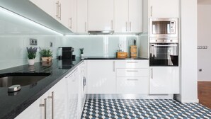 A modern kitchen with white cabinets, a black countertop, and a patterned floor. - Feel Porto DOC Townhouse (Porto)