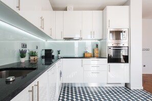 Una cocina moderna con armarios blancos, encimera negra y suelo estampado.