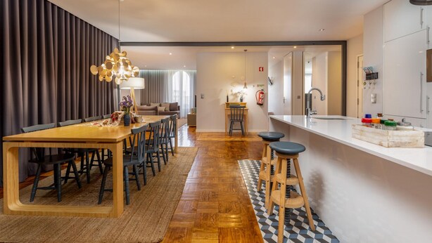 Eine moderne Küche mit Holztisch, Barhocker und weißer Arbeitsplatte.