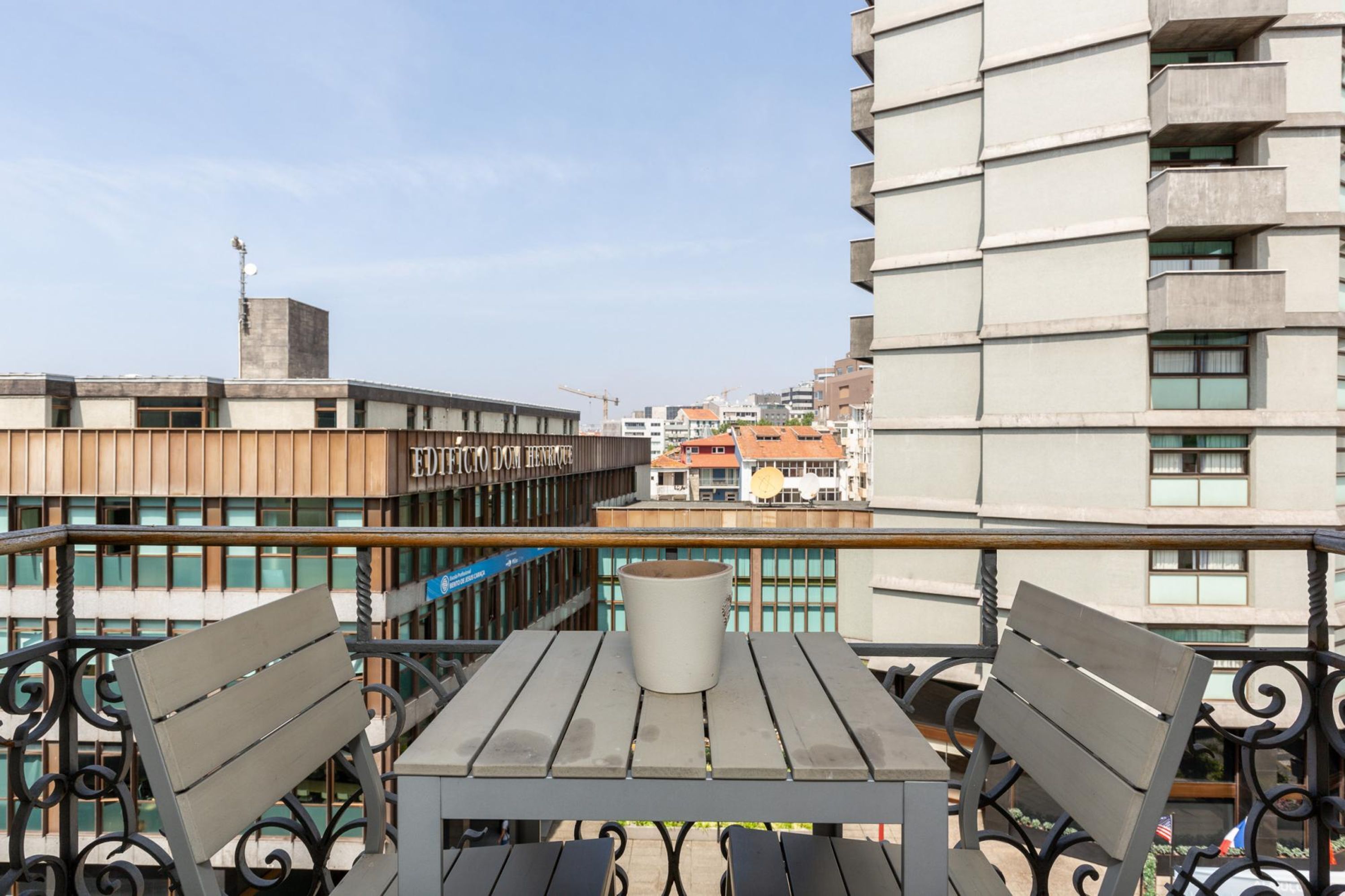 A balcony with a table and two chairs, overlooking a cityscape with modern buildings and a construction crane.