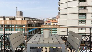 Ein Balkon mit Tisch und zwei Stühlen, mit Blick auf eine Skyline mit modernen Gebäuden und einem Baukran.