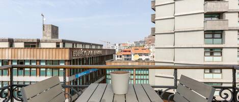 A balcony with a table and two chairs, overlooking a cityscape with modern buildings and a construction crane.
