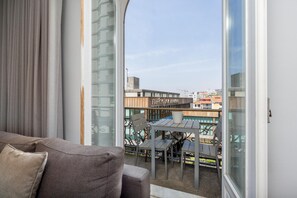 A balcony with a table and chairs, a sofa, and a view of buildings and a construction crane.