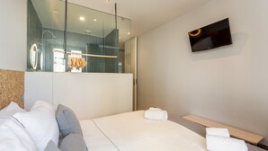 Ein modernes Hotelzimmer mit einem großen Bett, einem an der Wand montierten Fernseher und einer Duschkabine aus Glas.