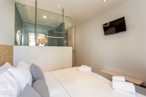 Ein modernes Hotelzimmer mit einem großen Bett, einem an der Wand montierten Fernseher und einer Duschkabine aus Glas.