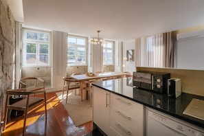Una cocina moderna con una isla central, zona de comedor con sillas y ventanas grandes.