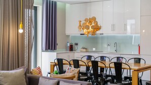 Une cuisine moderne avec des armoires blanches, un pare-feu en verre et un luminaire suspendu original.