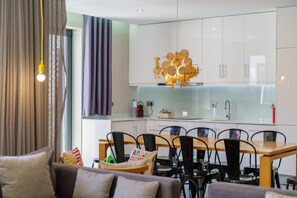 Une cuisine moderne avec des armoires blanches, un pare-feu en verre et un luminaire suspendu original.