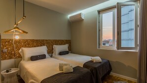 A hotel room with two beds, a hanging light fixture, an air conditioning unit, and a window with a city view. - Feel Porto Vintage Townhouse (Porto)