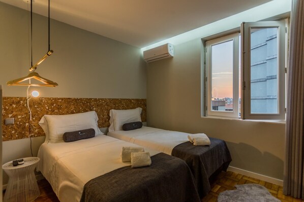 Une chambre d’hôtel avec deux lits, un luminaire suspendu, un appareil de climatisation et une fenêtre donnant sur la ville.