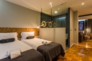 Une chambre d’hôtel moderne avec deux lits, un grand miroir et un petit coin salon.