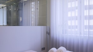 A modern bathroom with a glass shower enclosure, a bench, and rolled towels on a white surface. - Feel Porto Merlot Townhouse (Porto)