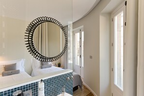 Un baño moderno con un espejo grande, un tocador con azulejos y una cama con sábanas blancas.