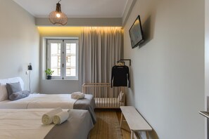 Une chambre d’hôtel moderne avec deux lits, un berceau, un banc, une télévision et une fenêtre avec des rideaux.