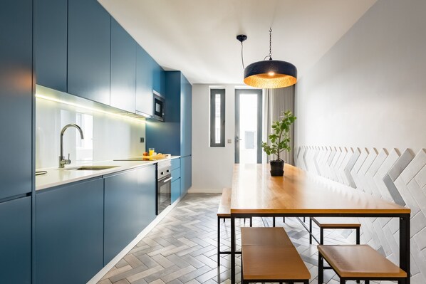 A modern kitchen with blue cabinets, a wooden dining table, and a hanging light fixture. - Feel Porto Merlot Townhouse (Porto)