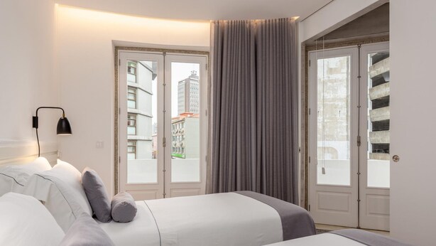 A hotel room with two beds, a large window with curtains, a door leading to a balcony, and a wall-mounted lamp. - Feel Porto Bacchus Townhouse (Porto)