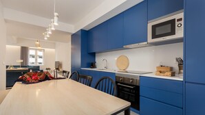 A modern kitchen with blue cabinets, a wooden dining table, and a microwave. - Feel Porto Bacchus Townhouse (Porto)
