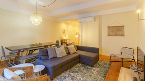 A modern living room with a grey sofa, a dining table, and wicker chairs. - Feel Porto Downtown Woods Flat (Porto)