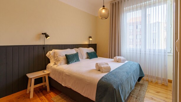A neatly made bed with white and teal bedding, a small wooden stool, and a hanging light fixture. - Feel Porto Downtown Woods Flat (Porto)