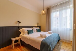 A neatly made bed with white and teal bedding, a small wooden stool, and a hanging light fixture. - Feel Porto Downtown Woods Flat (Porto)