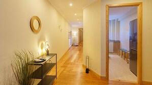 A hallway with a wooden floor, a small table with a lamp, and a mirror on the wall. - Feel Porto Downtown Woods Flat (Porto)