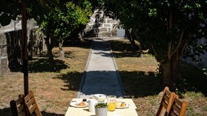 A table set outdoors with a checkered tablecloth, two wooden chairs, and a meal consisting of a croissant, a glass of orange juice, and a cup. - Feel Corporate Housing Marqu s I (Porto)