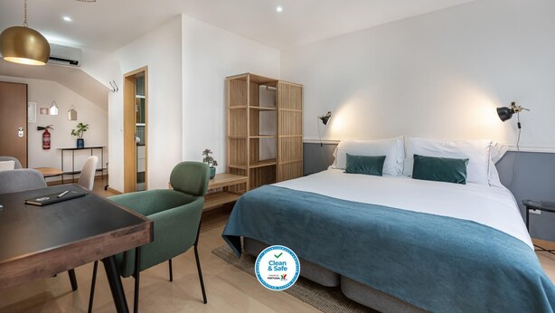 A modern hotel room with a large bed, a desk, a chair, a wardrobe, and a hanging light fixture. - Feel Corporate Housing Marqu s I (Porto)
