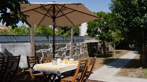 An outdoor dining area with a table set for four, surrounded by wooden chairs, under a beige umbrella. - Feel Corporate Housing Marqu s IV (Porto)