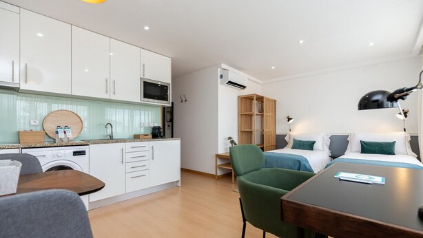 A modern hotel room with a kitchenette, a dining area, and a bed with green bedding. - Feel Corporate Housing Marqu s IV (Porto)
