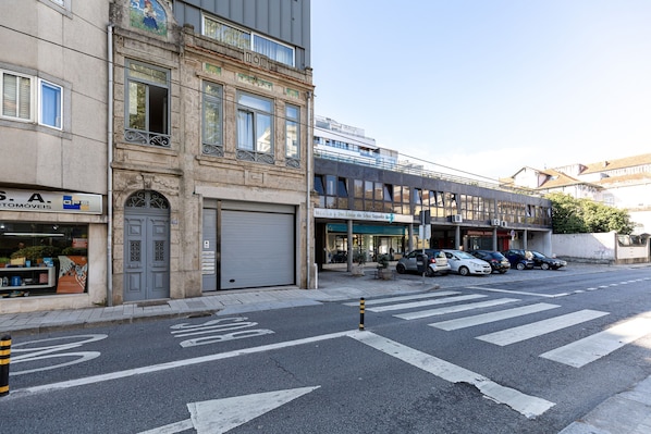 Vista de la calle con un edificio que tiene una puerta de garaje cerrada, una fila de coches aparcados y un cielo despejado.