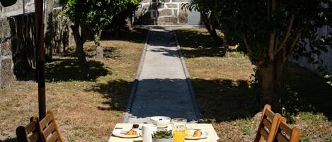 A table set outdoors with a checkered tablecloth, two wooden chairs, and a meal consisting of a croissant, a glass of orange juice, and a cup.