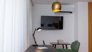 A modern room with a wooden desk, a green chair, a small table, a television, and a pendant light. - Feel Corporate Housing Marqu s V (Porto)