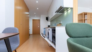 A compact kitchen with a dishwasher, a microwave, and a small countertop. There is a wooden cabinet and a green chair in the foreground. - Feel Corporate Housing Marqu s V (Porto)
