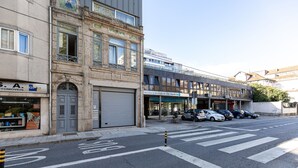 A street view with a building featuring a closed garage door, a row of parked cars, and a clear sky. - Feel Corporate Housing Marqu s V (Porto)