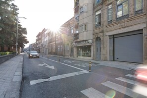 A street with a car driving, buildings with shops, and a clear sky.