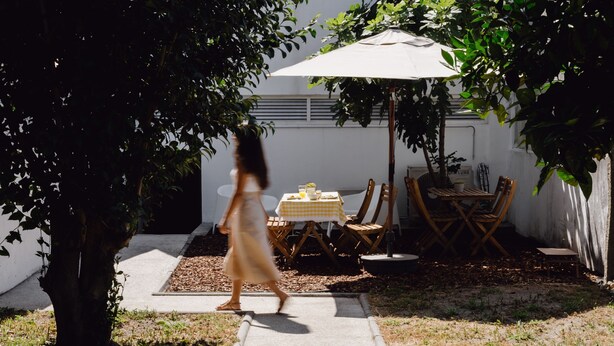 Un patio con mesa y sillas bajo un paraguas grande, rodeado de árboles.